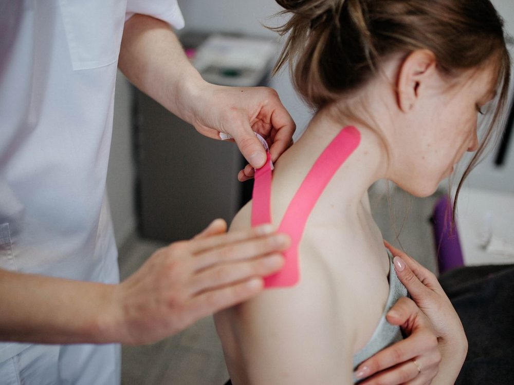 Anlegen eines elastischen Kinesio-Tapes auf Nacken und Schulter einer Patientin