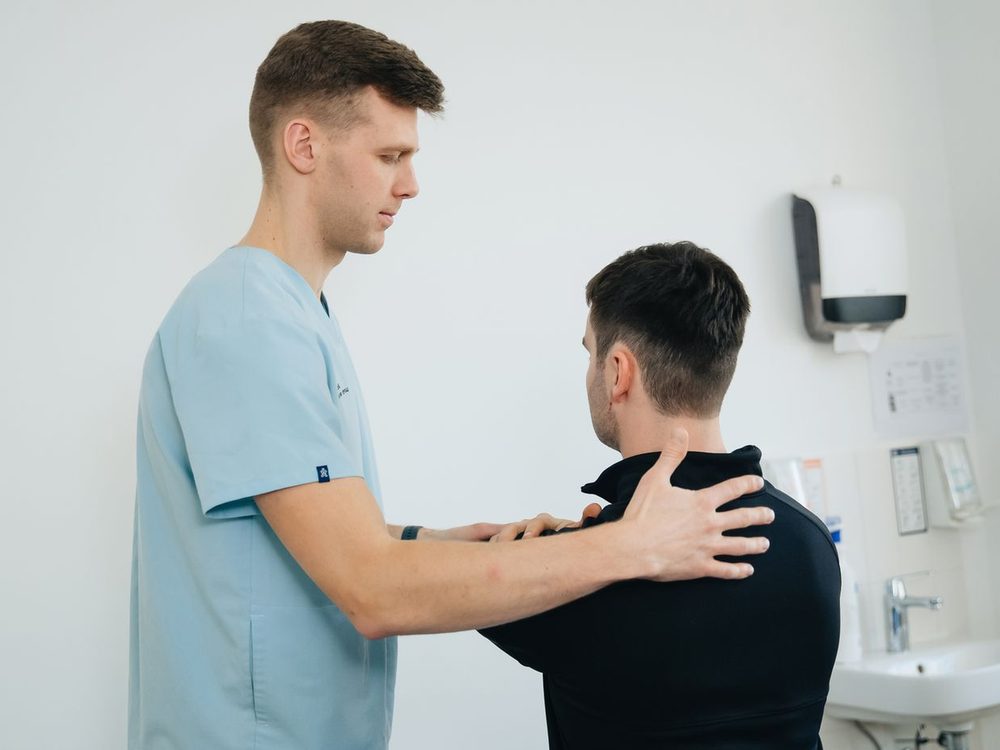 Physiotherapeut behandelt mit den Händen die Schulter eines Patienten im Behandlungsraum